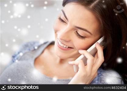 people, technology, winter, christmas and communication concept - close up of happy young woman calling on smartphone at home over snow