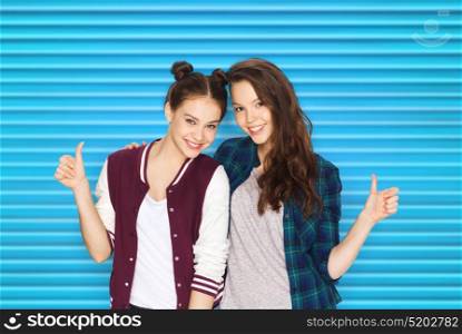 people, teens and friendship concept - happy smiling pretty teenage girls or friends hugging and showing thumbs up over blue ribbed background. happy smiling teenage girls showing thumbs up
