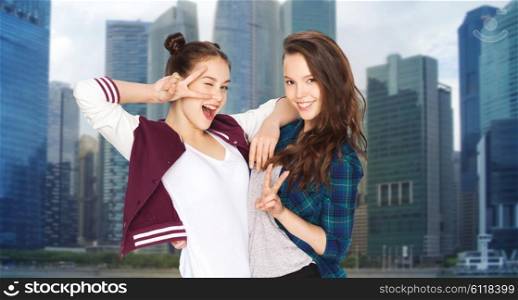 people, teens, friendship, travel and tourism concept - happy smiling pretty teenage girls showing peace hand sign over singapore city background