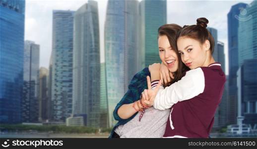 people, teens, friendship, travel and tourism concept - happy smiling pretty teenage girls hugging and showing peace hand sign over singapore city background