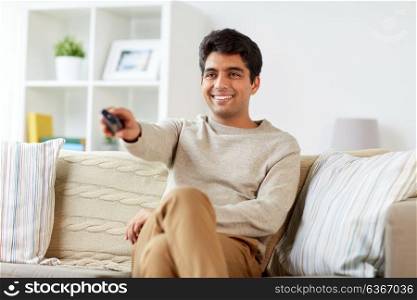 people, television and entertainment concept - man with remote control watching tv at home. man with remote control watching tv at home
