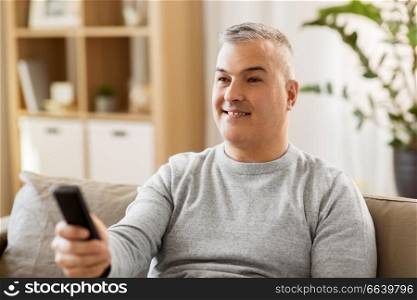 people, television and entertainment concept - man with remote control watching tv at home. man with remote control watching tv at home
