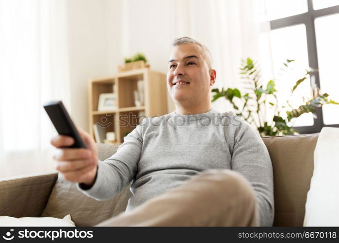 people, television and entertainment concept - smiling man with remote control watching tv at home. man with remote control watching tv at home. man with remote control watching tv at home