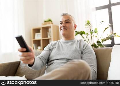 people, television and entertainment concept - smiling man with remote control watching tv at home. man with remote control watching tv at home. man with remote control watching tv at home
