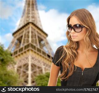 people, tourism and travel concept - beautiful young woman in shades over eiffel tower and blue sky background