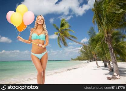 people, travel and summer holidays concept - happy smiling young woman in bikini swimsuit holding air balloons over exotic tropical beach with palm trees background. happy woman in bikini with air balloons on beach