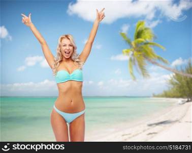 people, travel and summer holidays concept - happy smiling young woman in bikini swimsuit with raised hands over exotic tropical beach and palm trees background. happy woman in bikini with raised hands on beach