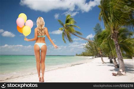 people, travel and summer holidays concept - young woman in bikini swimsuit holding air balloons from back over exotic tropical beach with palm trees background. woman in bikini with air balloons on beach