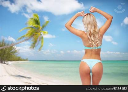 people, travel and summer holidays concept - young woman in bikini swimsuit from back over exotic tropical beach with palm trees background. woman in bikini swimsuit from back on beach