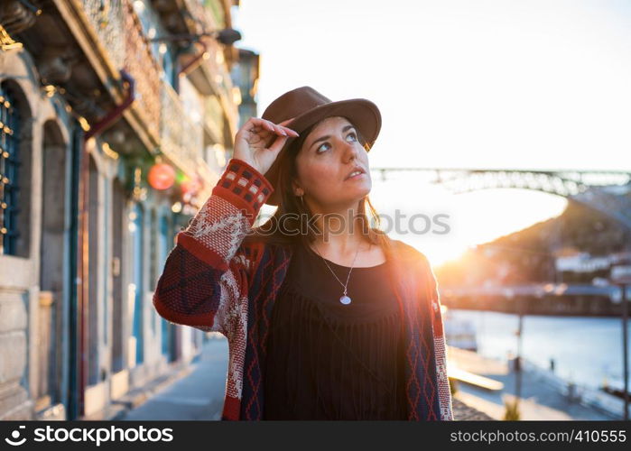 People, travel, holidays and adventure concept. Young woman with long hair walking on city street at sunrise, wearing hat and coat, enjoying happy pleasant moment of her vacations. Young woman with long hair walking on city street at sunrise, wearing hat and coat, enjoying happy pleasant moment of her vacations