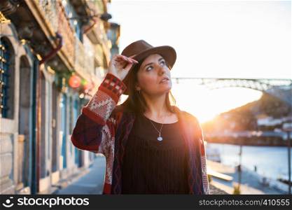 People, travel, holidays and adventure concept. Young woman with long hair walking on city street at sunrise, wearing hat and coat, enjoying happy pleasant moment of her vacations. Young woman with long hair walking on city street at sunrise, wearing hat and coat, enjoying happy pleasant moment of her vacations