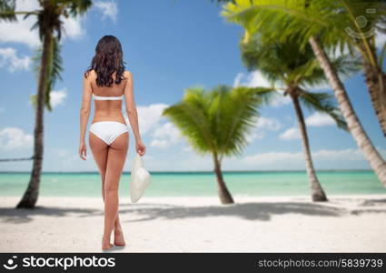 people, travel, swimwear, summer and beauty concept - young woman in white bikini swimsuit from back over tropical beach with palm trees background