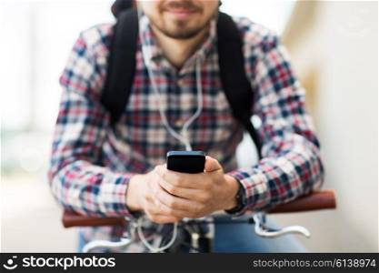 people, travel, technology, leisure and lifestyle - close up of young hipster man in earphones with smartphone and fixed gear bike listening to music on city street