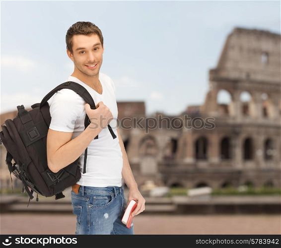 people, travel, tourism and education concept - happy young man with backpack and book travelling over coliseum background