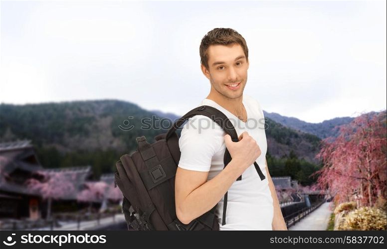 people, travel, tourism and education concept - happy young man with backpack and book travelling over asian landscape background