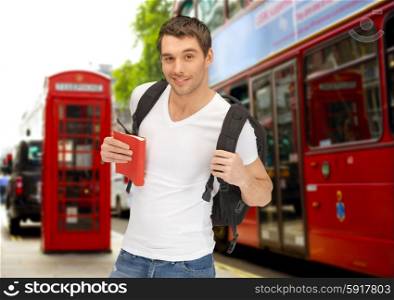 people, travel, tourism and education concept - happy young man with backpack and book over london city bus on street background