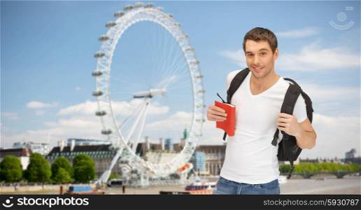 people, travel, tourism and education concept - happy young man with backpack and book over london ferry wheel background