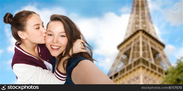 people, travel, tourism and friendship concept - happy smiling pretty teenage girls taking selfie and kissing over eiffel tower in paris background