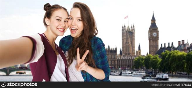 people, travel, tourism and friendship concept - happy smiling pretty teenage girls taking selfie and showing peace sign over london background