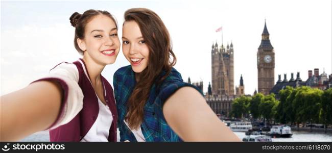 people, travel, tourism and friendship concept - happy smiling pretty teenage girls taking selfie over london background