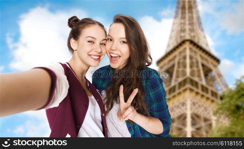 people, travel, tourism and friendship concept - happy smiling pretty teenage girls taking selfie and showing peace sign over eiffel tower in paris background