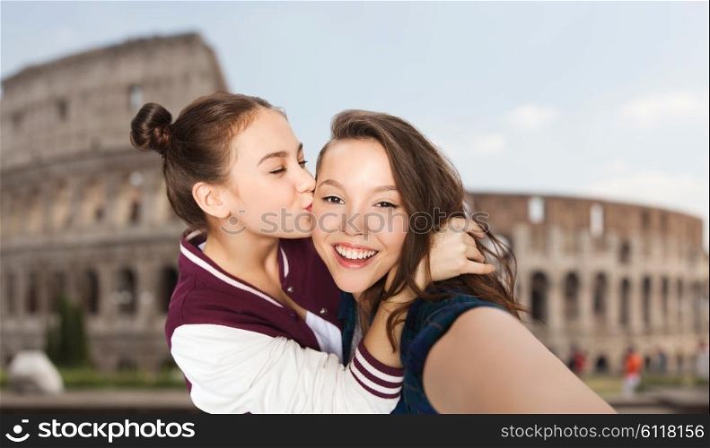 people, travel, tourism and friendship concept - happy smiling pretty teenage girls taking selfie and kissing over coliseum in rome background