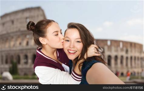 people, travel, tourism and friendship concept - happy smiling pretty teenage girls taking selfie and kissing over coliseum in rome background