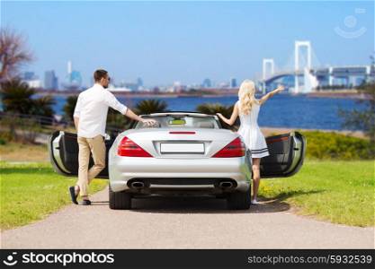 people, travel, tourism and road trip concept - happy man and woman near cabriolet car over river and tokyo rainbow bridge background