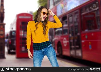 people, travel, tourism, style and fashion concept - happy young woman or teen girl in casual clothes and sunglasses having fun over london city street background