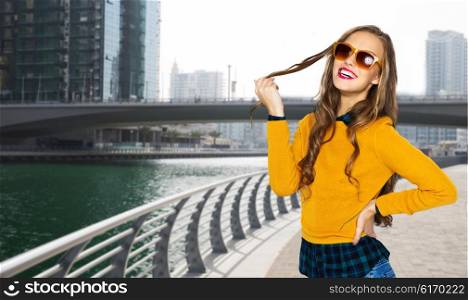 people, travel, tourism, style and fashion concept - happy young woman or teen girl in casual clothes and sunglasses over dubai city street background