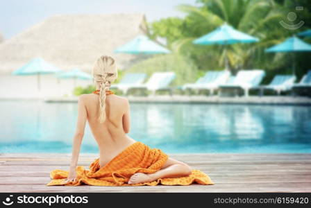 people, travel, tourism, summer vacation and people concept - woman with orange towel from back over exotic hotel resort beach with swimming pool and sunbeds background