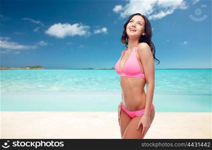 people, travel, tourism, swimwear and summer holidays concept - happy young woman in pink bikini swimsuit over exotic tropical beach background
