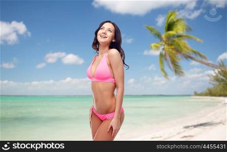 people, travel, tourism, swimwear and summer holidays concept - happy young woman in pink bikini swimsuit over exotic tropical beach with palm trees background