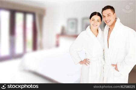 people, travel, tourism, vacation and honeymoon concept - happy couple in bathrobes over spa hotel room background