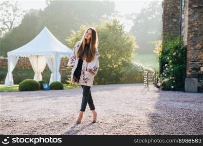 People, travelling and excursions concept. Tall young female stands crossed legs outdoors, has walk in ancient area near old builduings or landmarks, admires beautiful landscapes which surround her