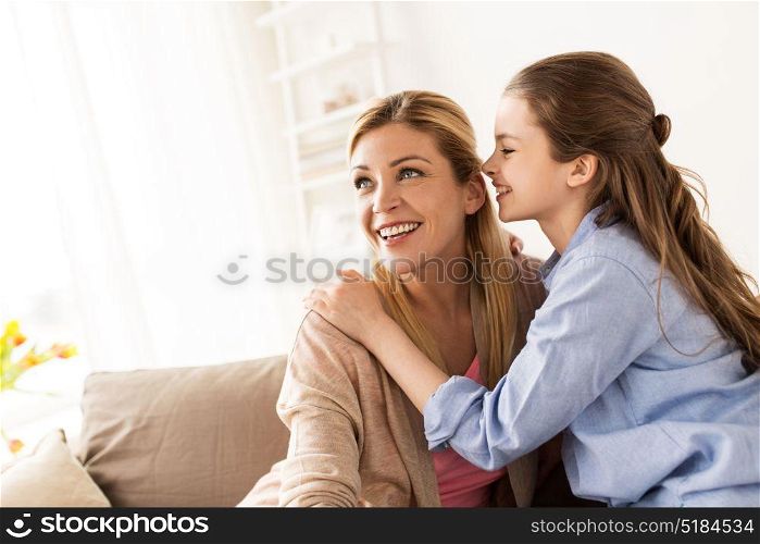people, trust and family concept - happy daughter whispering secret to her mother at home. happy girl whispering secret to her mother at home