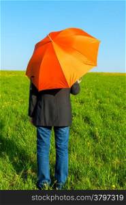people under an orange umbrella in a field waiting for rain
