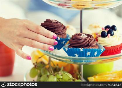 people, unhealthy eating and junk food concept - close up of hand taking cupcake from cake stand. close up of hand taking cupcake from cake stand. close up of hand taking cupcake from cake stand