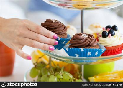 people, unhealthy eating and junk food concept - close up of hand taking cupcake from cake stand