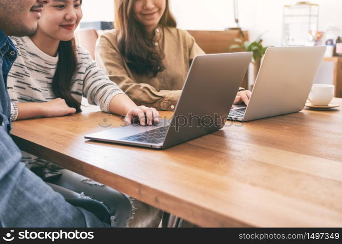 People using and looking at laptop computer on wooden table together