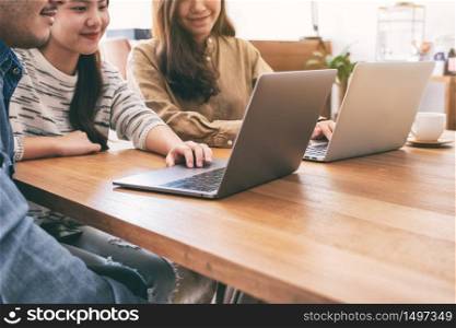 People using and looking at laptop computer on wooden table together