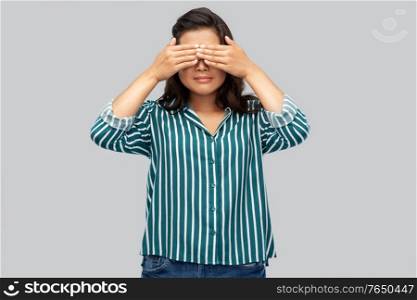people, vision and expression concept - young woman with eyes closed by hands over grey background. woman with eyes closed by hands