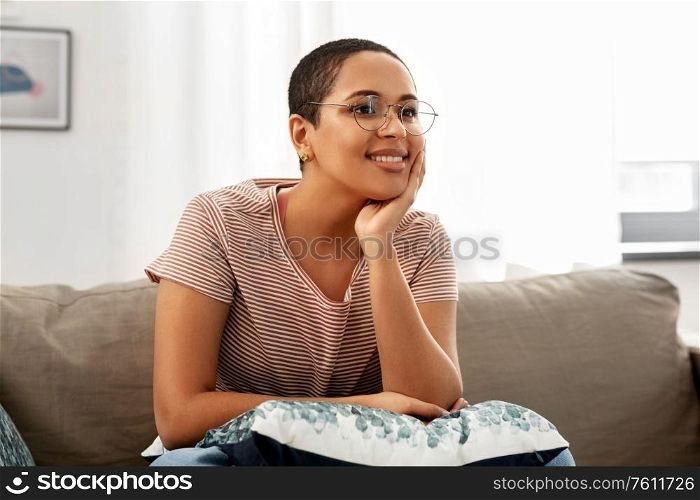people, vision and leisure concept - happy smiling african american woman in glasses sitting on sofa at home. african american woman in glasses sitting on sofa