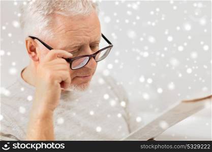 people, vision and mass media concept - close up of senior man in glasses reading newspaper at home over snow. close up of old man in glasses reading newspaper