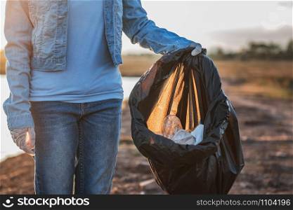 people volunteer keeping garbage plastic and glass bottle into black bag at park river in sunset