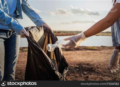 people volunteer keeping garbage plastic bottle into black bag at park near river in sunset