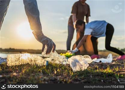 people volunteer keeping garbage plastic bottle into black bag at park near river in sunset