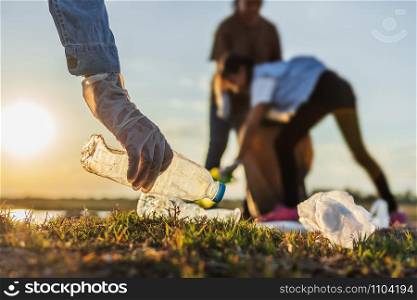 people volunteer keeping garbage plastic bottle into black bag at park river in sunset