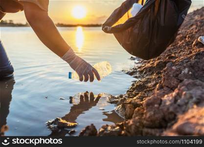 people volunteer keeping garbage plastic bottle into black bag on river in sunset