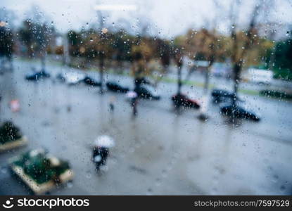 people walk in the rain on the street, view through a wet window